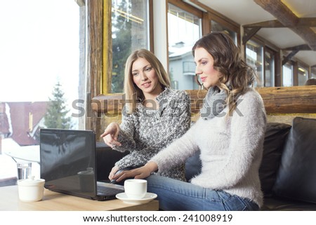 Two girlfriends drinking coffee in the cafe and surfing the web