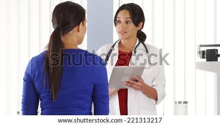 Hispanic physician using tablet computer talking to Black patient