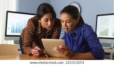 African American business women working on tablet computer with hispanic colleague
