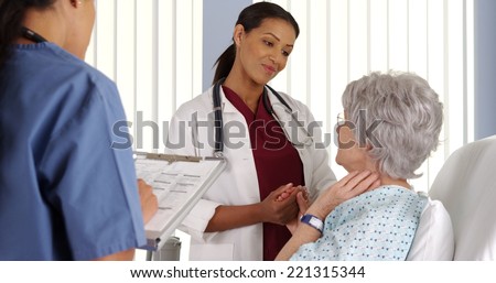 Black woman doctor holding elderly patient\'s hand in hospital room