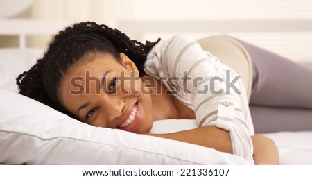 Cute african woman lying on bed looking at camera