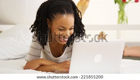 Smiling black woman using laptop on bed