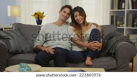 Sweet mixed race couple sitting on couch smiling