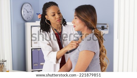 African American doctor listening to heart and lungs of Asian patient
