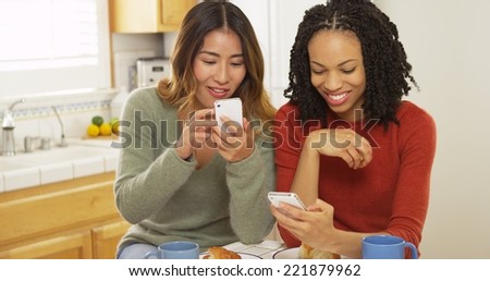 African American and Asian friends using mobile phones and eating breakfast