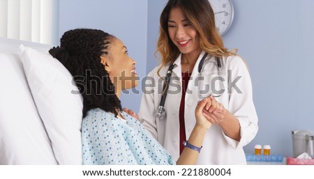 Japanese doctor holding hand of black woman patient in hospital