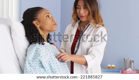 Japanese doctor listening to heart and lungs of black patient in bed