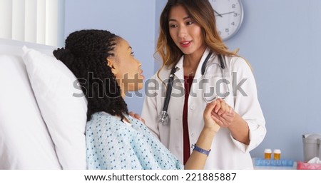 Asian doctor holding hand of black woman patient in hospital bed