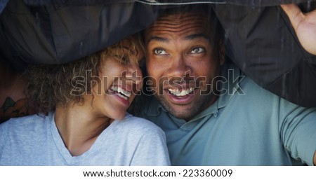Black couple standing under coat trying not to get wet