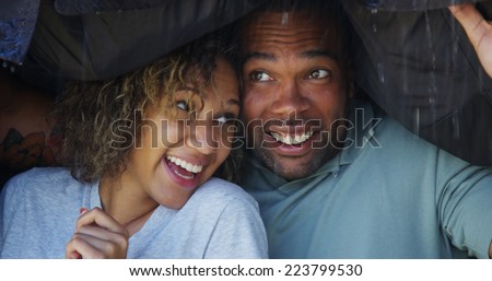 Black couple standing under coat trying not to get wet