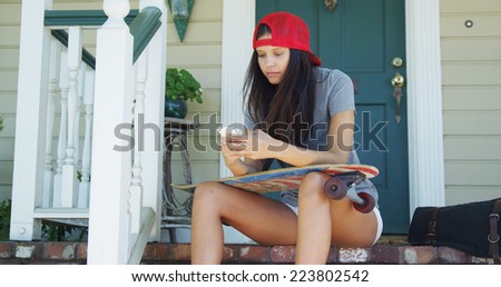 Mixed race woman sitting on porch with skateboard texting