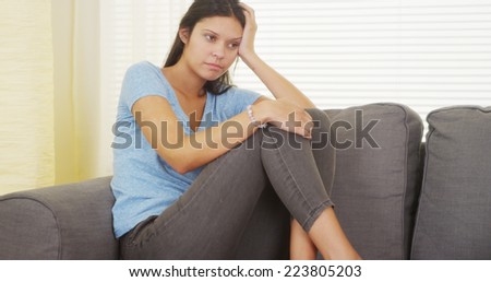 Hispanic woman sitting on couch thinking