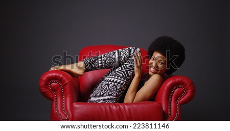 African woman in red leather arm chair kicking legs playfully