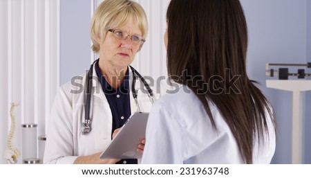 mature doctor taking notes on tablet while talking to patient