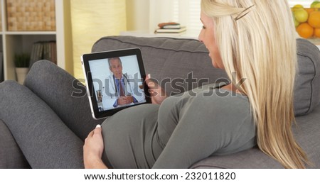 Beautiful Pregnant woman happily chatting with doctor on tablet