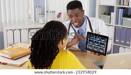 African American doctor using tablet to show ultrasound to patient at desk