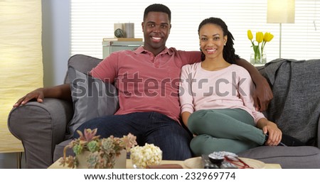 Smiling young black couple sitting on sofa looking at camera