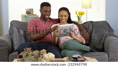 Smiling young black couple using tablet computer on couch