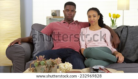 Attractive young black couple sitting on couch looking at camera