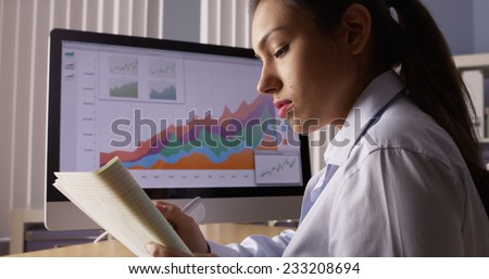 Hispanic businesswoman writing notes by computer