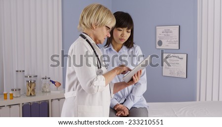 Senior doctor taking notes on tablet while talking to patient