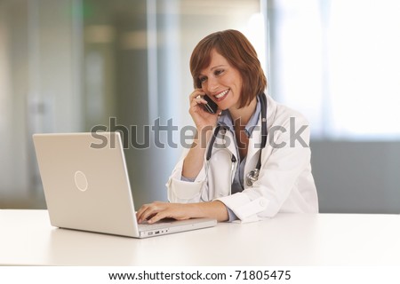 Portrait of young woman doctor in white coat at computer using phone