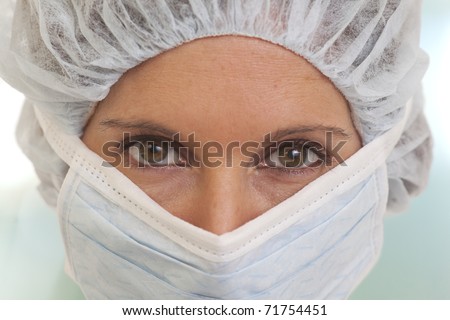 Portrait of serious young woman doctor in scrubs with mask and cap
