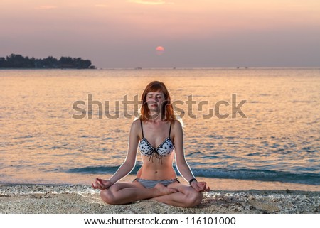 Woman in yoga lotus meditation position back to seaside at sunset