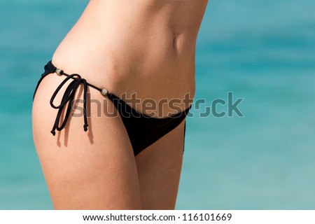 Closeup of slim woman belly in black bikini on water background