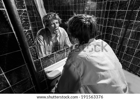Drunk Man looks at himself in the mirror in a bathroom. grayscale image
