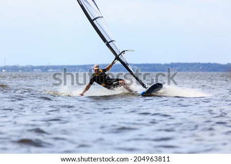 Young man surfing the wind and touching water surface with splashes