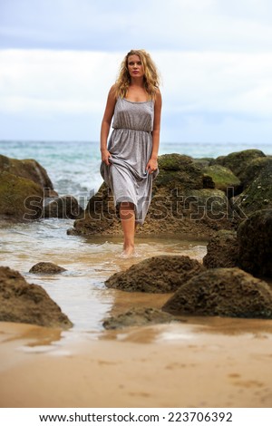 Blonde Woman in Long Dress Posing at the beach with cloudy blue sky