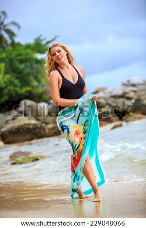 Blonde Woman in Black Swimsuit Walking  At The Beach And Smiling In Camera. Tilt Horizon