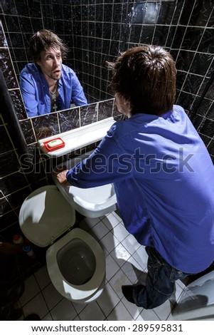 Drunk Man looks at himself in the mirror in a bathroom. Color image