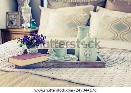Vintage photo of decorative tray with book,tea set and flower on the bed