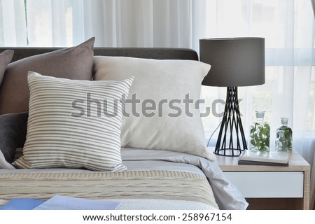 stylish bedroom interior design with brown patterned pillows on bed and decorative table lamp.