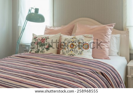 vintage bedroom interior with flower pillows and pink striped blanket on bed