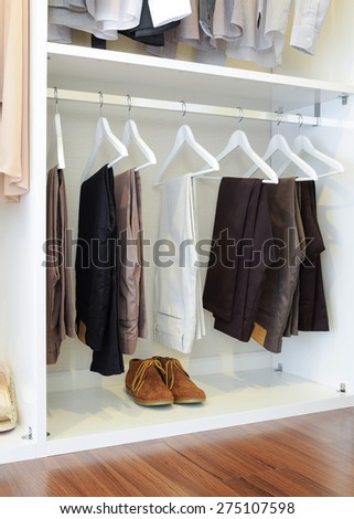 brown leather shoes and row of black pants hangs in wardrobe