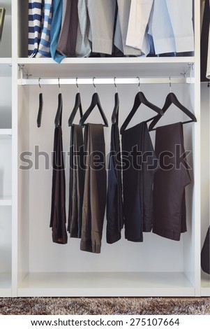 modern closet with row of pants hanging in white wardrobe