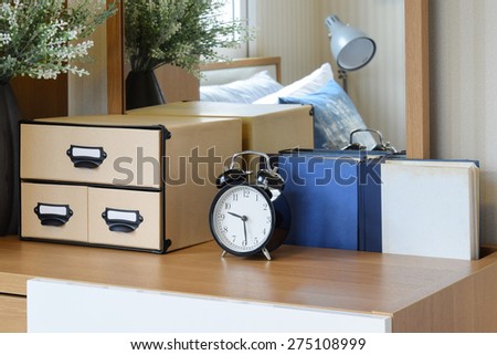 black alarm clock on wooden table in cozy bedroom interior