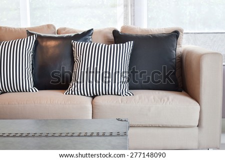 Striped and black leather pillows on velvet beige sofa in modern industrial style living room