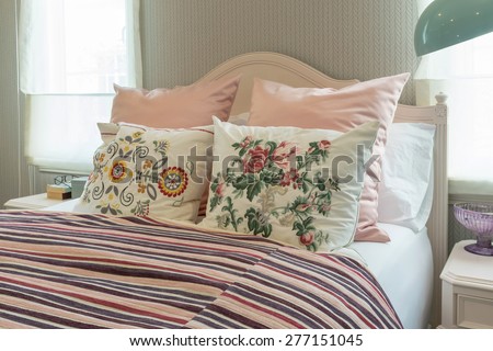 vintage bedroom interior with flower pillows and pink striped blanket on bed