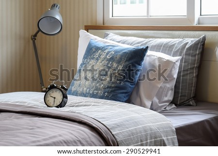 black alarm clock in cozy bedroom interior with pillows and reading lamp
