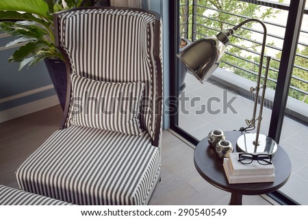 black striped easy chair in the corner with decorative brass lamp and books on wooden round table