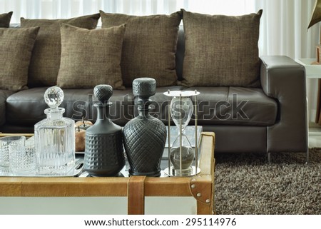 Crystal drink set and sandglass on glass top table with wooden frame and dark brown sofa set in the living room