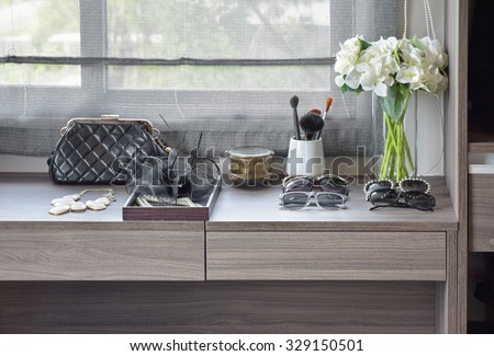 handbag,sunglasses,jewelry and makeup brushes on a wooden dressing table