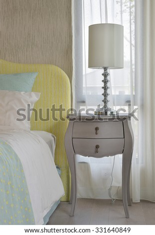 Classic style bedside table with reading lamp next to cozy style bedding with many style of green and yellow pillows
