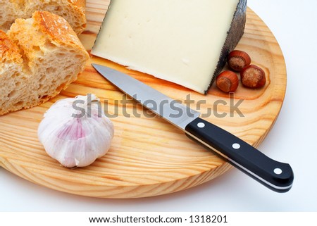 Cheese, bread, hazelnuts and knife on wood plate over a white background