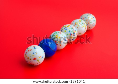 One blue ball amongst five white balls, Focus on blue ball with shallow DOF, red background