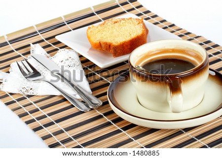 Close-up of a sponge cake with the spoon inside cup of coffee, knife and fork